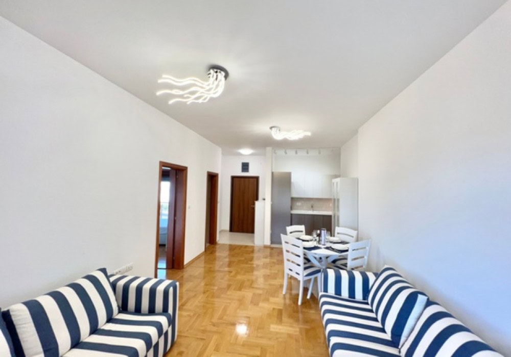 Wohnzimmer mit gestreiften Sofas und Essbereich in einer Wohnung in Bečići, Montenegro: modernes Interieur mit Parkett.