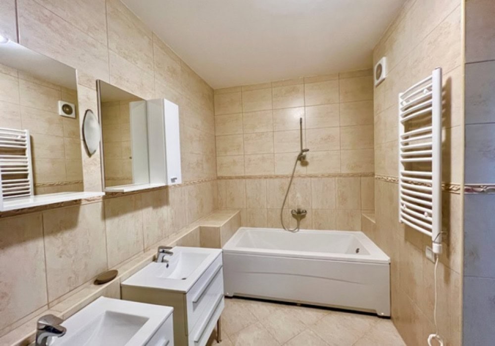 Badezimmer in der Wohnung, Bečići, Montenegro: beige Fliesen, Badewanne, Waschtisch und Handtuchheizkörper.