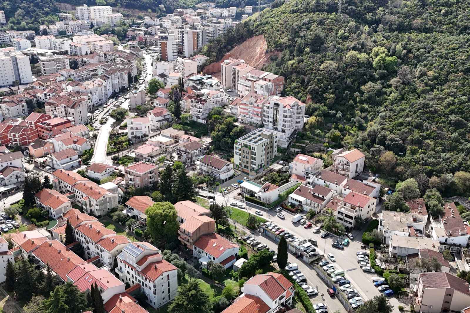 Luftaufnahme eines dicht besiedelten Stadtgebiets mit Wohngebäuden und üppiger grüner Hügelvegetation