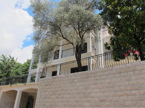 Weiße Villa in Budva, Montenegro: Fassade mit schmiedeeisernen Balkonen, Stein-Stützmauer und Olivenbaum.