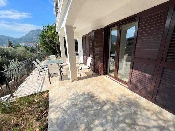 Geräumige Terrasse der Villa in Budva, Montenegro, mit Gartenmöbeln, Panoramablick auf die Berge und braunen Fensterläden.