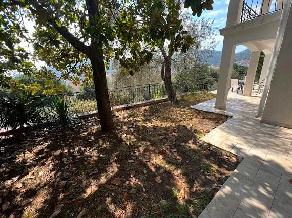 Terrasse einer Villa in Budva, Montenegro: Blick auf den Garten mit Bäumen, gepflasterte Fläche und schmiedeeisernes Grundstücksgeländer.