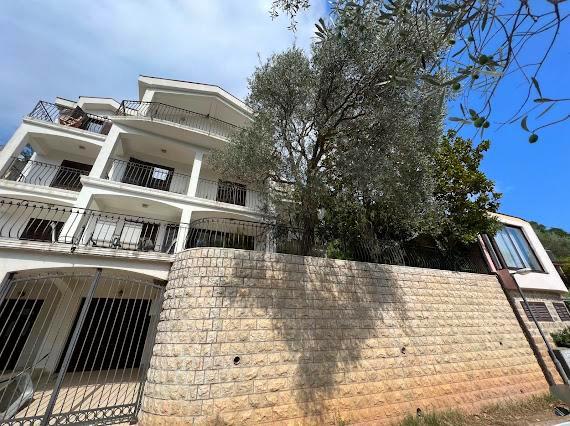 Dreistöckige Villa in Budva, Montenegro: Fassade mit Balkonen, Stein-Stützmauer und Olivenbaum am Eingang.