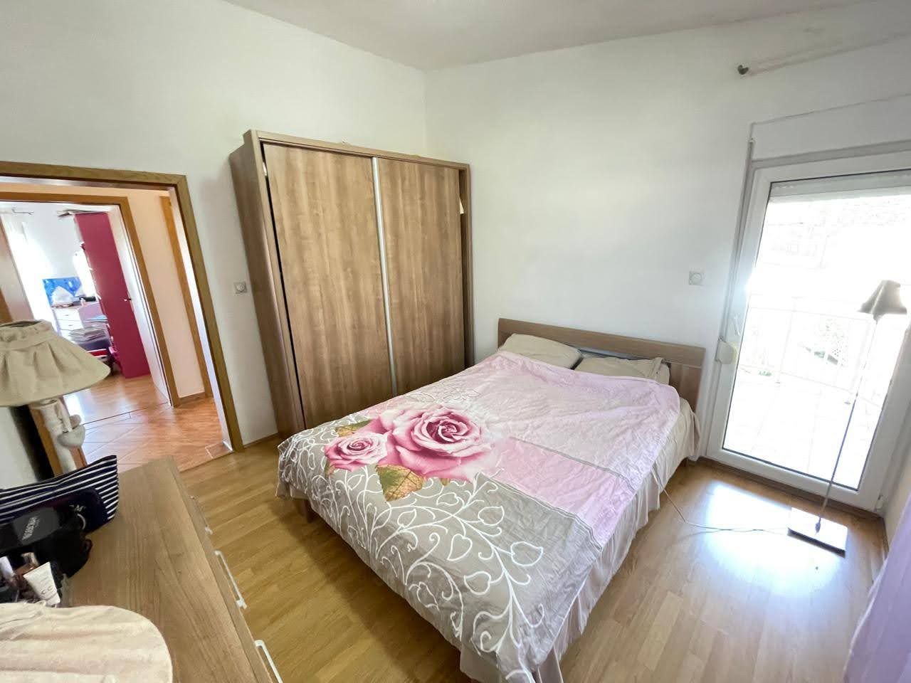 Aydınlık yatak odası, çift kişilik yatak ve dolap ile satılık evde, Bar şehri, Karadağ. Balkon ve koridora manzara.