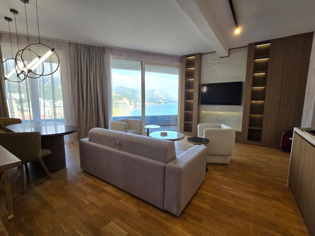 Modernes Wohnzimmer mit Meerblick in einer Wohnung, Bečići, Montenegro: helle Möbel, Parkett und Panoramafenster.