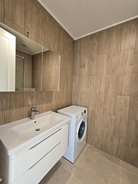 Modernes Badezimmer in einer Wohnung in Bečići, Montenegro: weiße Waschtischanlage, Waschmaschine und Holzoptik-Fliesen.