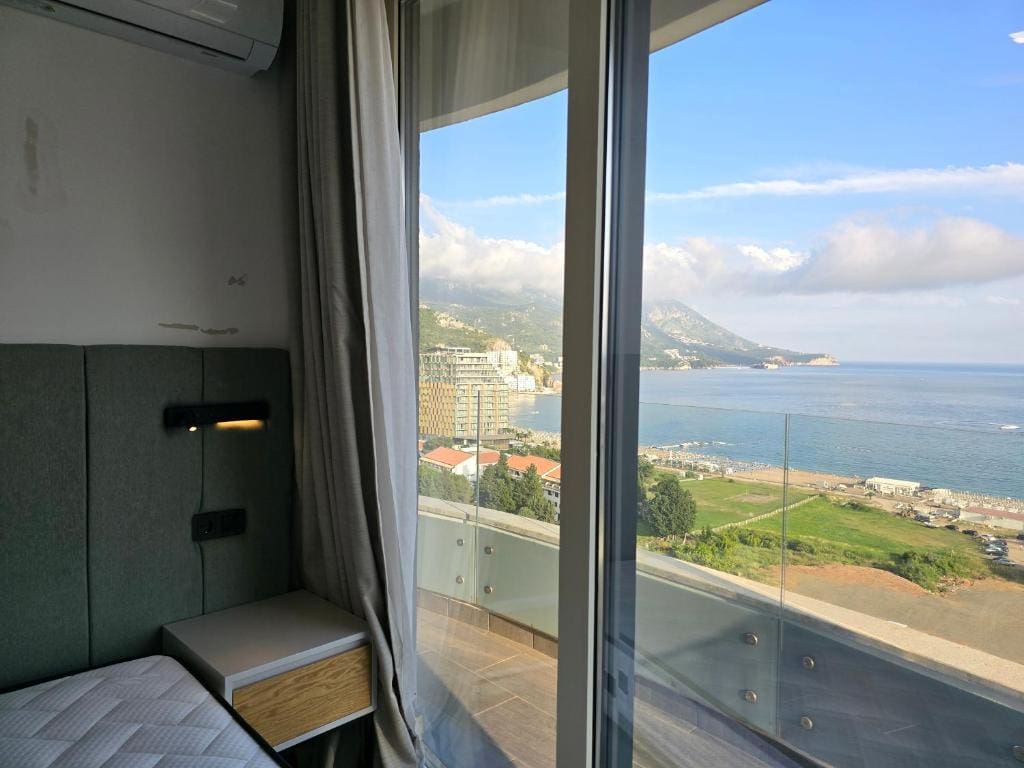 Schlafzimmer mit Panoramablick auf das Meer und die Berge in einer Wohnung, Bečići, Montenegro. Moderne Ausstattung und Balkon mit Glasgeländer.
