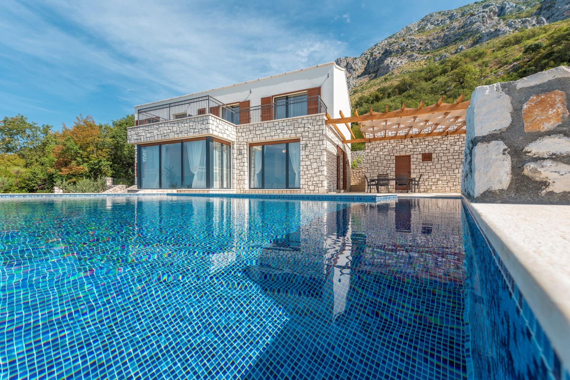 Villa moderne avec piscine et parement en pierre à Reževići, Monténégro : vue sur la maison avec terrasse et montagnes.