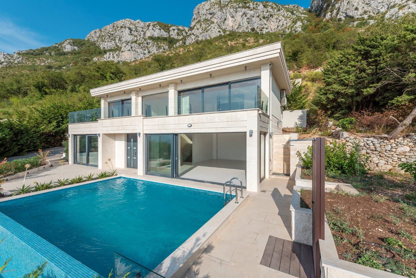 Villa moderne avec piscine et baies vitrées panoramiques à Reževići, Monténégro : vue sur la maison au pied des montagnes.
