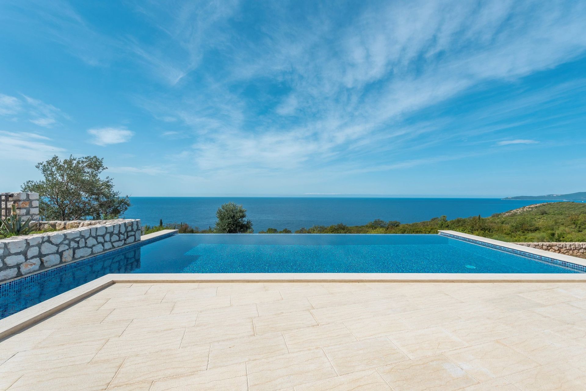 Piscine à débordement avec vue sur la mer près de la maison à Reževići, Monténégro : terrasse en pierre et panorama marin.