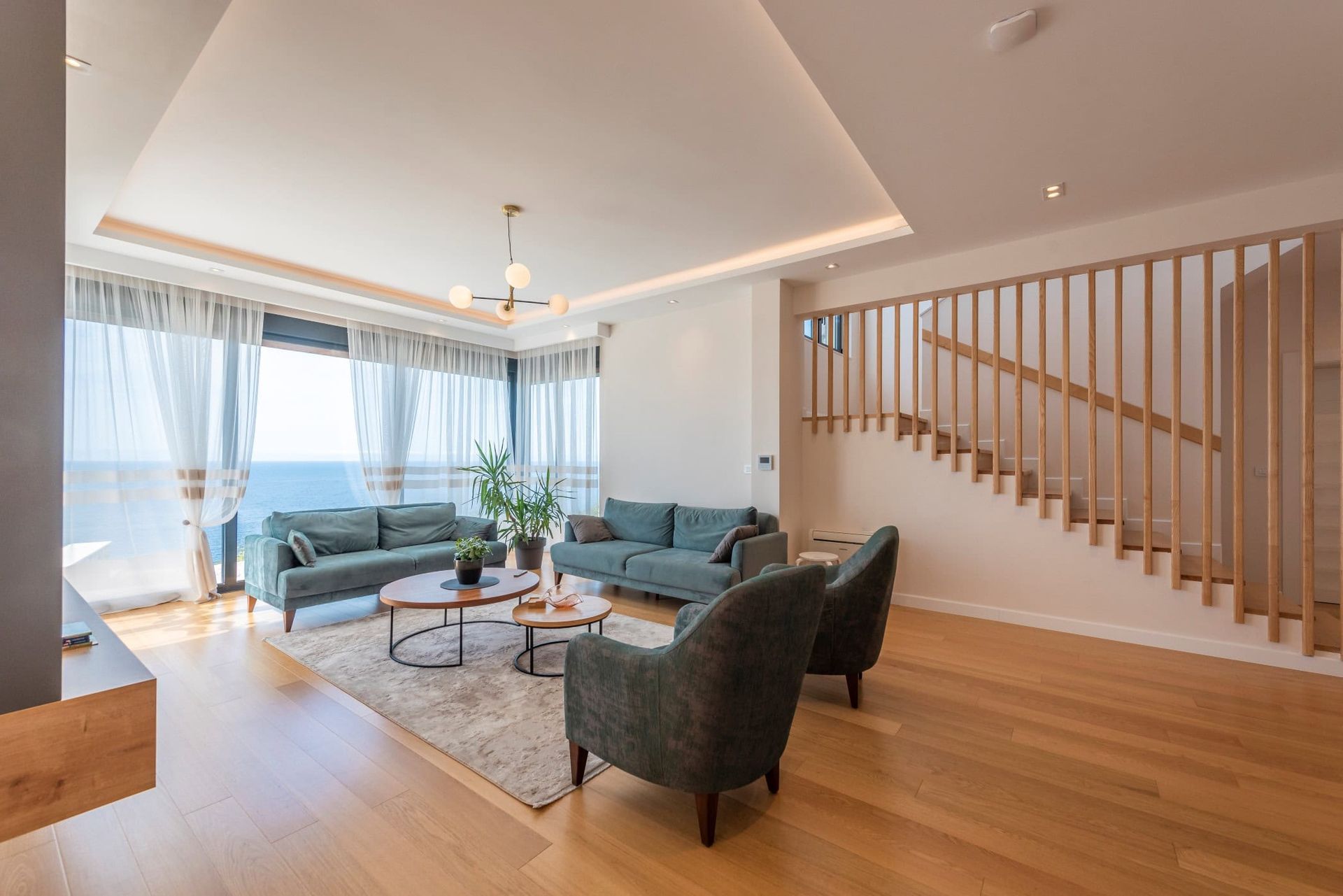 Salon moderne dans une maison à Reževići, Monténégro : vue panoramique sur la mer, mobilier moelleux et escalier en bois.