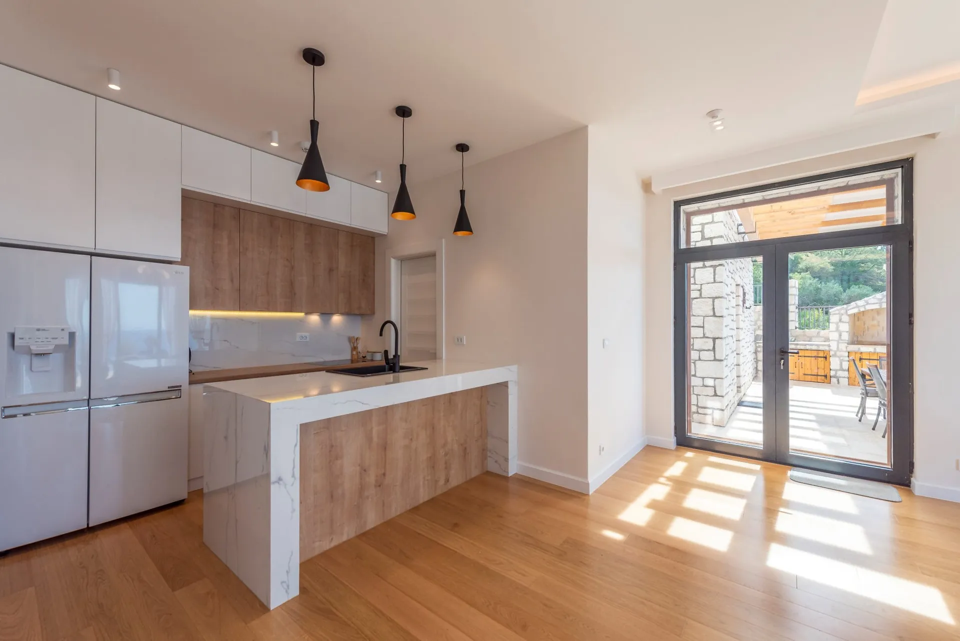 Cuisine moderne avec îlot dans une maison à Reževići, Monténégro : meubles clairs, plan de travail en marbre et accès à la terrasse.