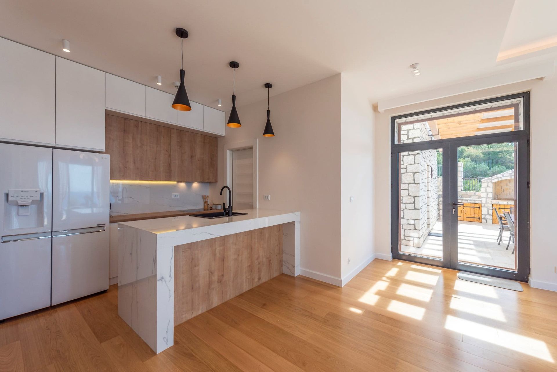 Cuisine moderne avec îlot dans une maison à Reževići, Monténégro : meubles clairs, plan de travail en marbre et accès à la terrasse.