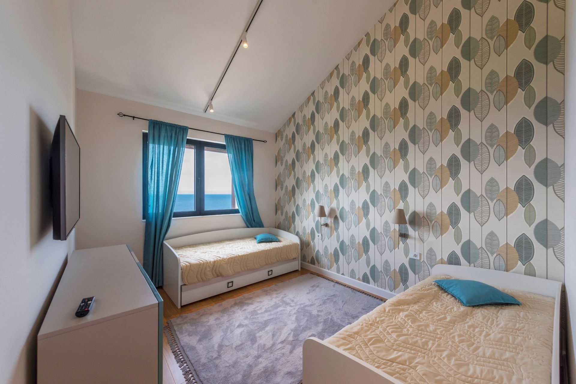 Chambre avec deux lits, papier peint à motifs et vue sur la mer dans une maison, Reževići, Monténégro.