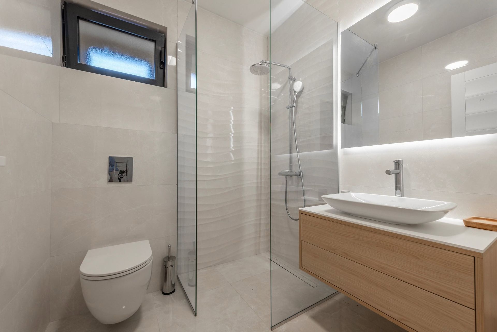 Salle de bains moderne dans une maison, Reževići, Monténégro : cabine de douche, meuble suspendu et finition claire en carrelage.