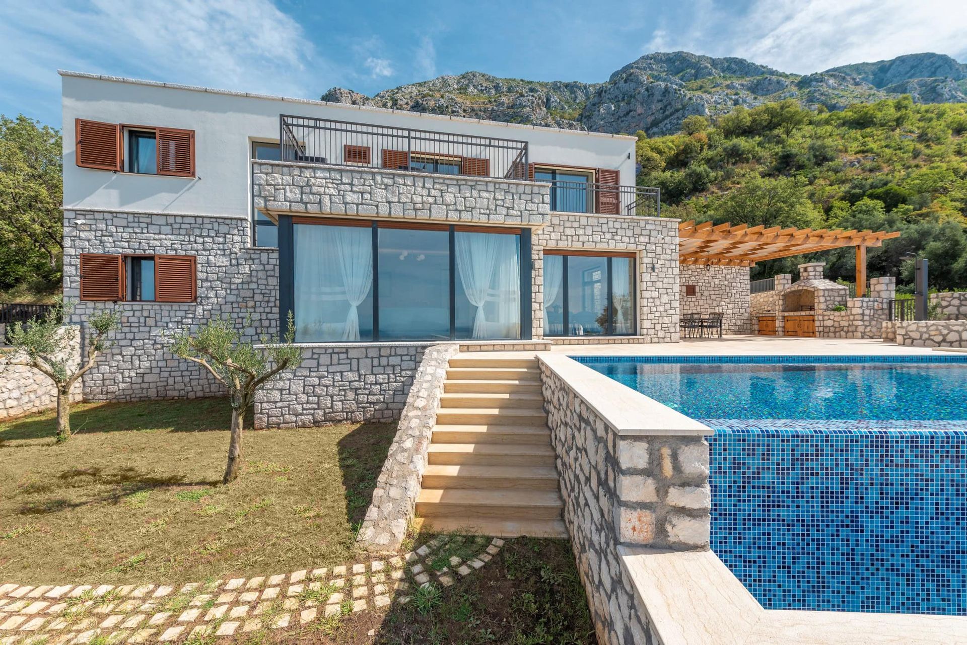Villa moderne à Reževići, Monténégro : parement en pierre, baies panoramiques, piscine et espace barbecue avec vue sur les montagnes.