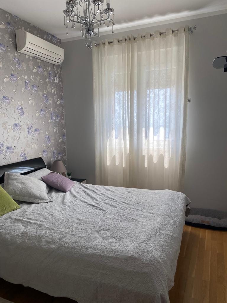 Gemütliches Schlafzimmer mit Doppelbett in einer Wohnung in Bečići, Montenegro: Tapete mit Blumenmuster, Klimaanlage und Parkett.