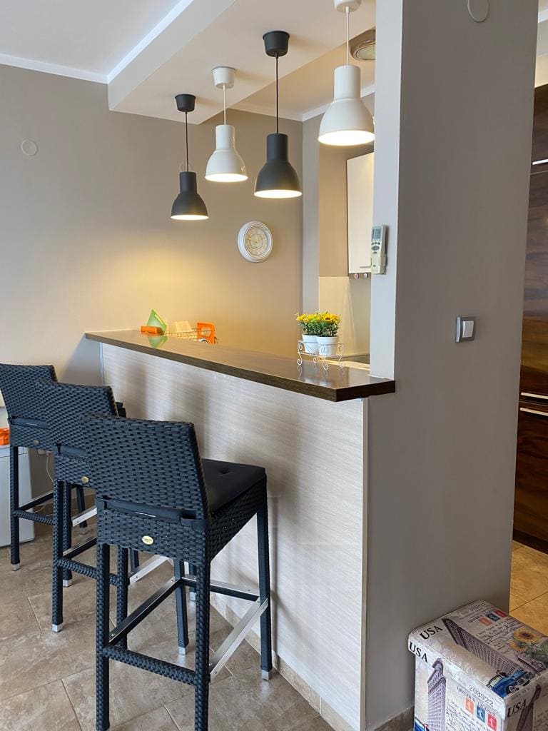 Moderne Küche mit Bartheke und geflochtenen Stühlen in einer Wohnung, Bečići, Montenegro. Stilvolles Interieur mit Beleuchtung.