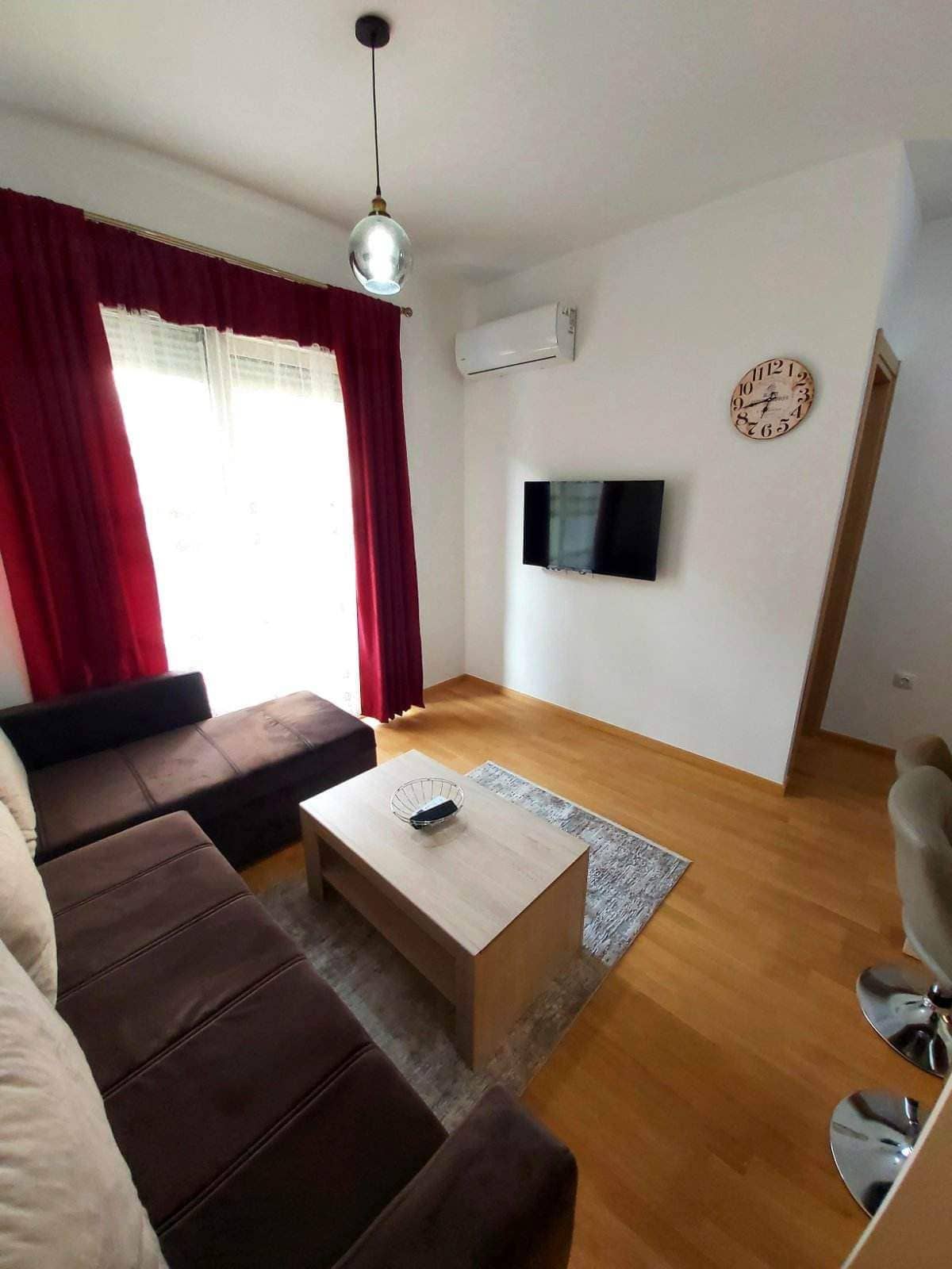 Gemütliches Wohnzimmer mit braunem Sofa und TV in einer zum Verkauf stehenden Wohnung in Budva, Montenegro: modernes Interieur und Parkett.