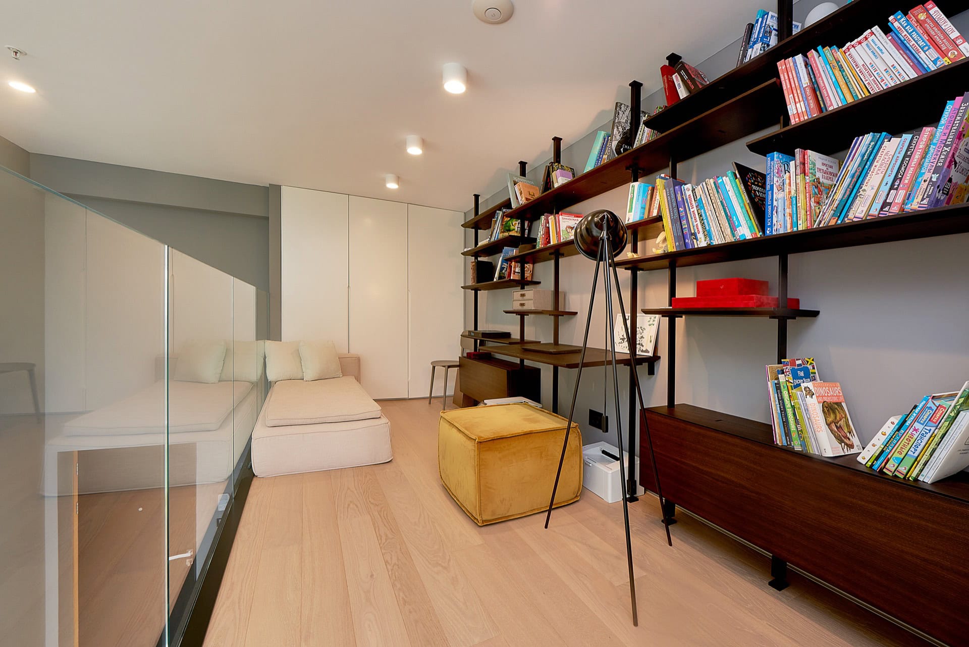 Gemütliches Wohnzimmer mit Bibliothek und Ruhebereich in einer Wohnung, Budva, Montenegro: helles Interieur, Regale und ein weicher Pouf.
