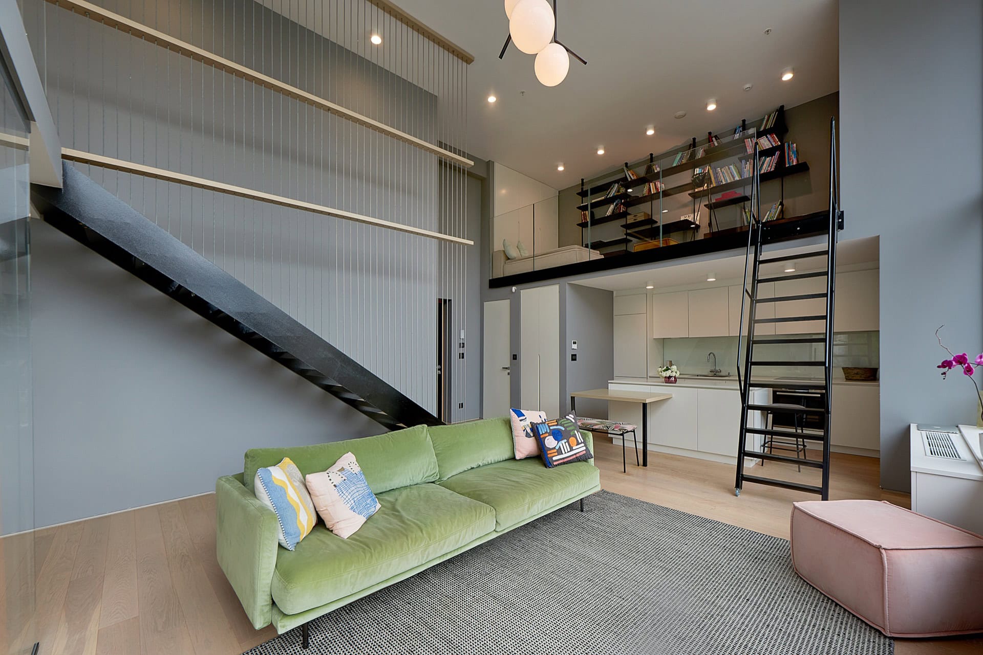 Moderne Maisonettewohnung in Budva, Montenegro: Wohnzimmer mit grünem Sofa, Küche und Treppe zur Galerie.