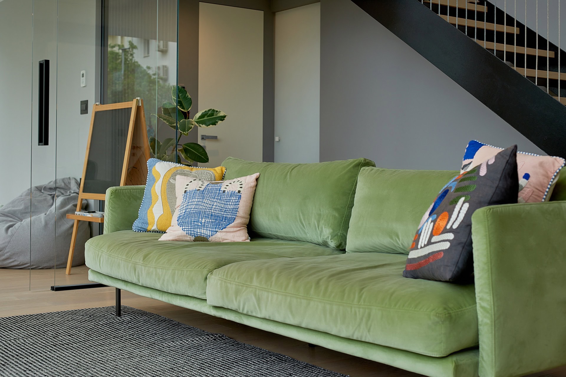 Grünes Samtsofa in einem modernen Wohnzimmer einer Wohnung im Zentrum von Budva, Montenegro, mit Treppe und Glasabtrennung.