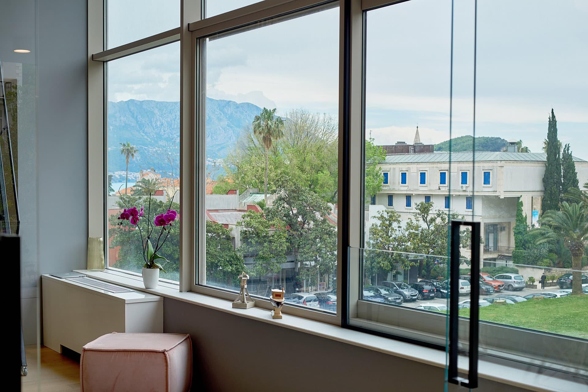 Blick aus den Panoramafenstern des Wohnzimmers auf die Berge und die Stadt Budva, Montenegro. Modernes Interieur mit einem rosa Pouf.