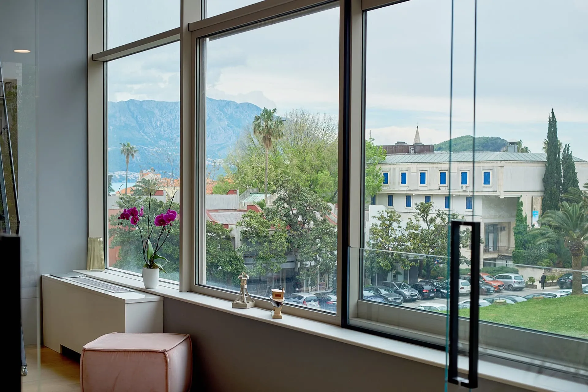 Pogled iz panoramskih prozora dnevne sobe na planine i grad Budvu, Crna Gora. Moderan enterijer sa roze tabureom.