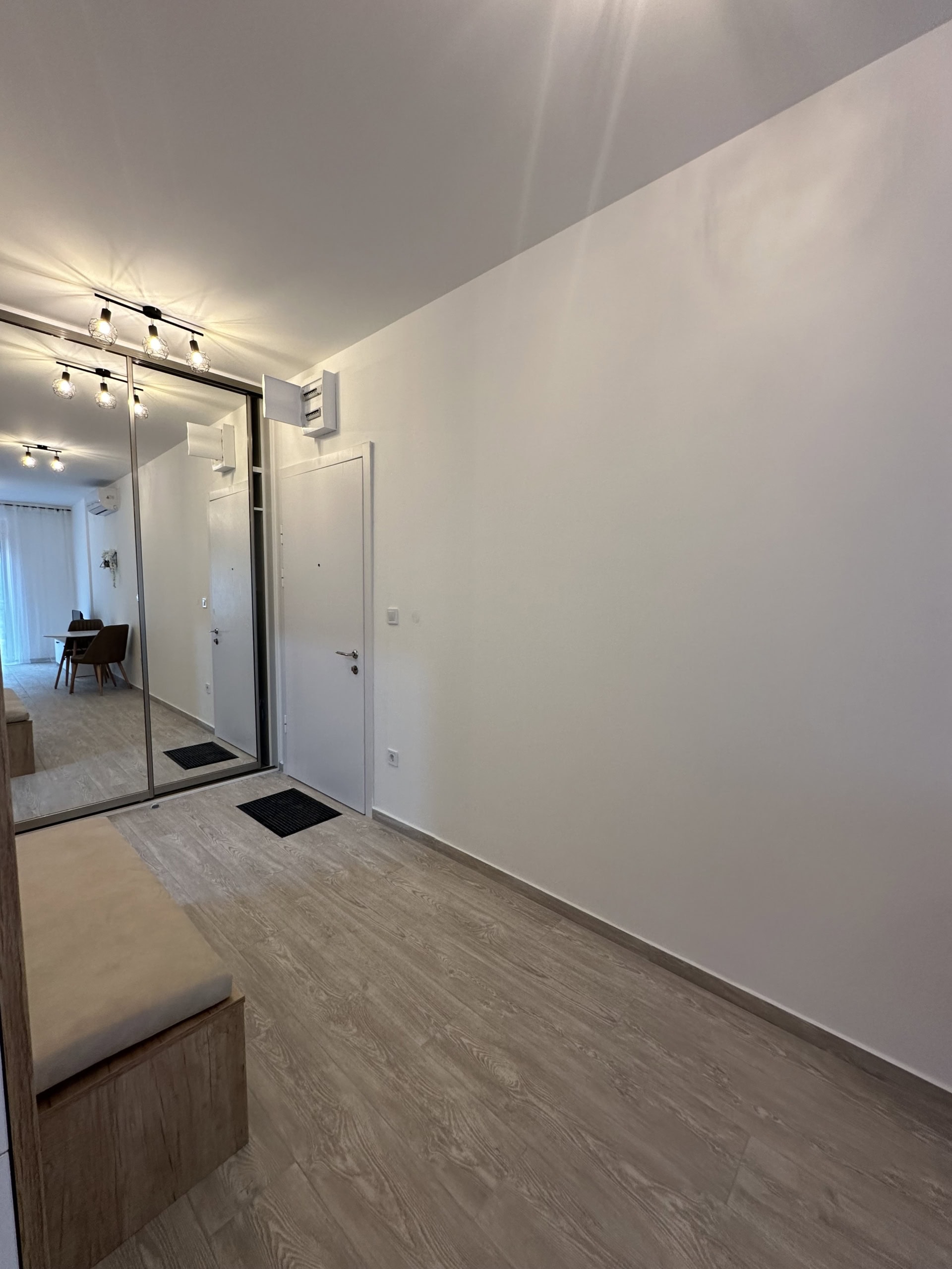 Flur in einer modernen Wohnung in Bečići, Montenegro: Spiegel-Schiebetürenschrank, helle Ausstattung und Laminat in Holzoptik.
