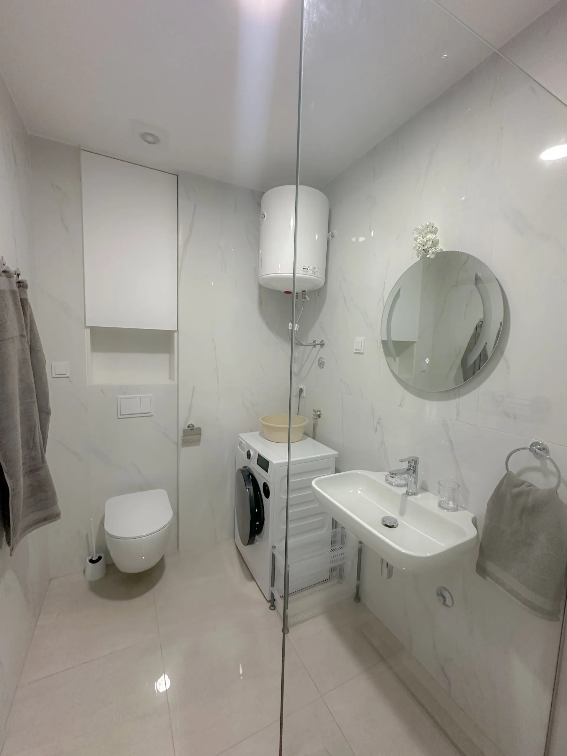 Modernes Badezimmer in einer Wohnung in Bečići, Montenegro: helle Fliesen, Hänge-WC, Waschbecken und Waschmaschine.