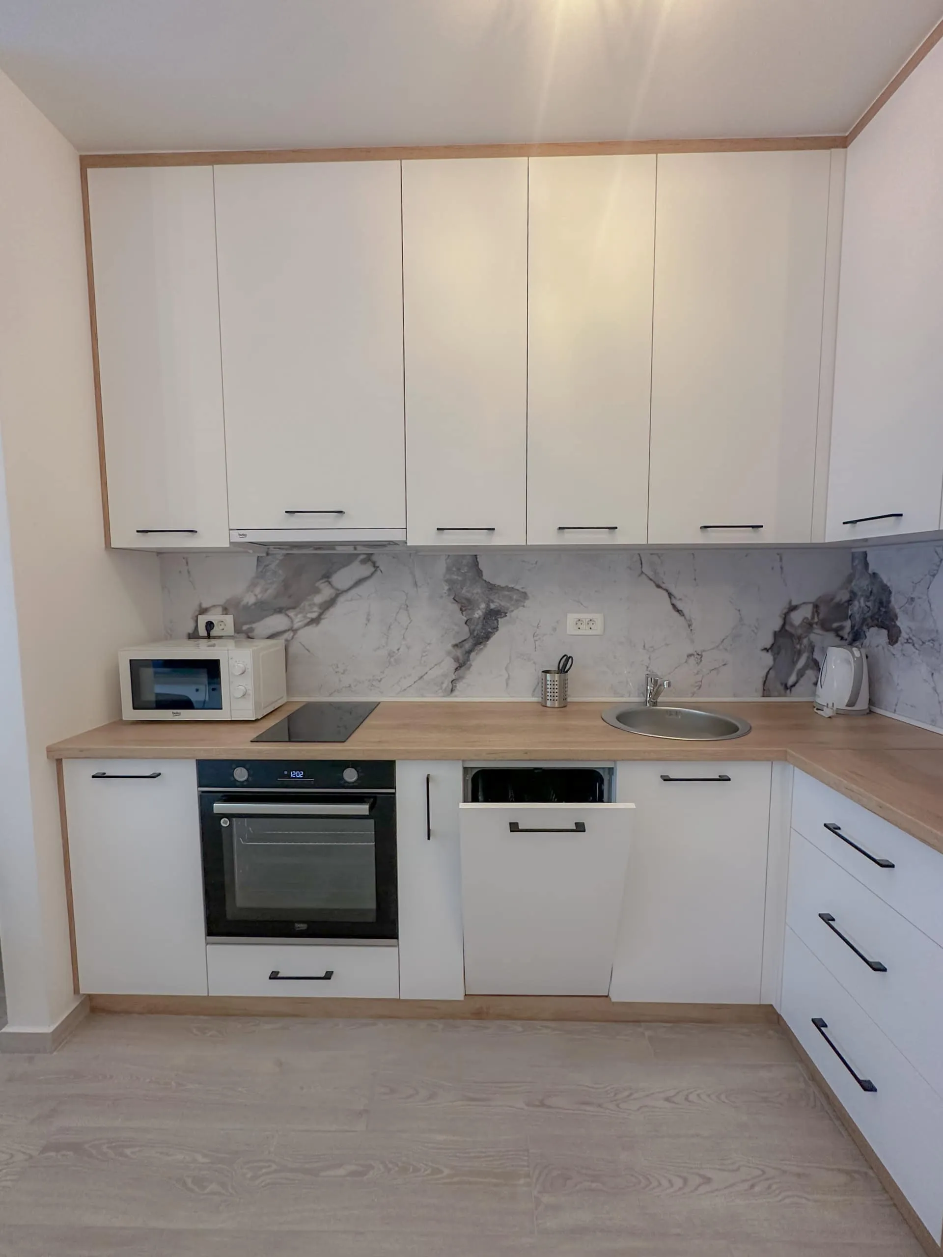 Moderne weiße Küche mit Marmor-Spritzschutz und Einbaugeräten in einer Wohnung, Bečići, Montenegro.