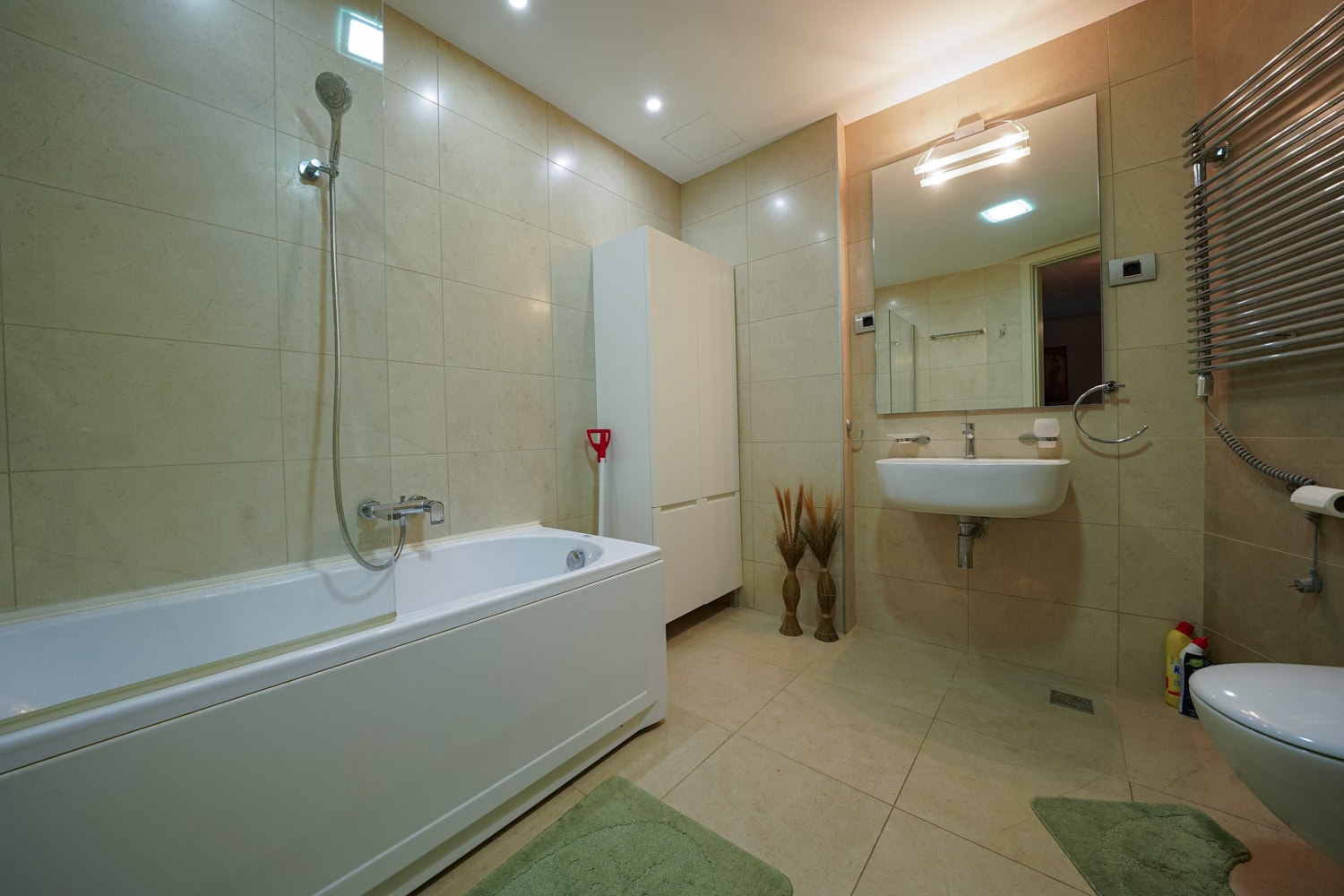 Modernes Badezimmer in einer Wohnung in Budva, Montenegro: weiße Sanitärkeramik, beige Fliesen und ein Handtuchheizkörper.