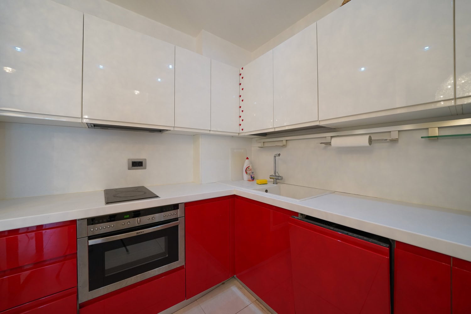 Moderne Küche mit roten und weißen Fronten in einer Wohnung in Budva, Montenegro: Einbaugeräte und helle Arbeitsplatte.