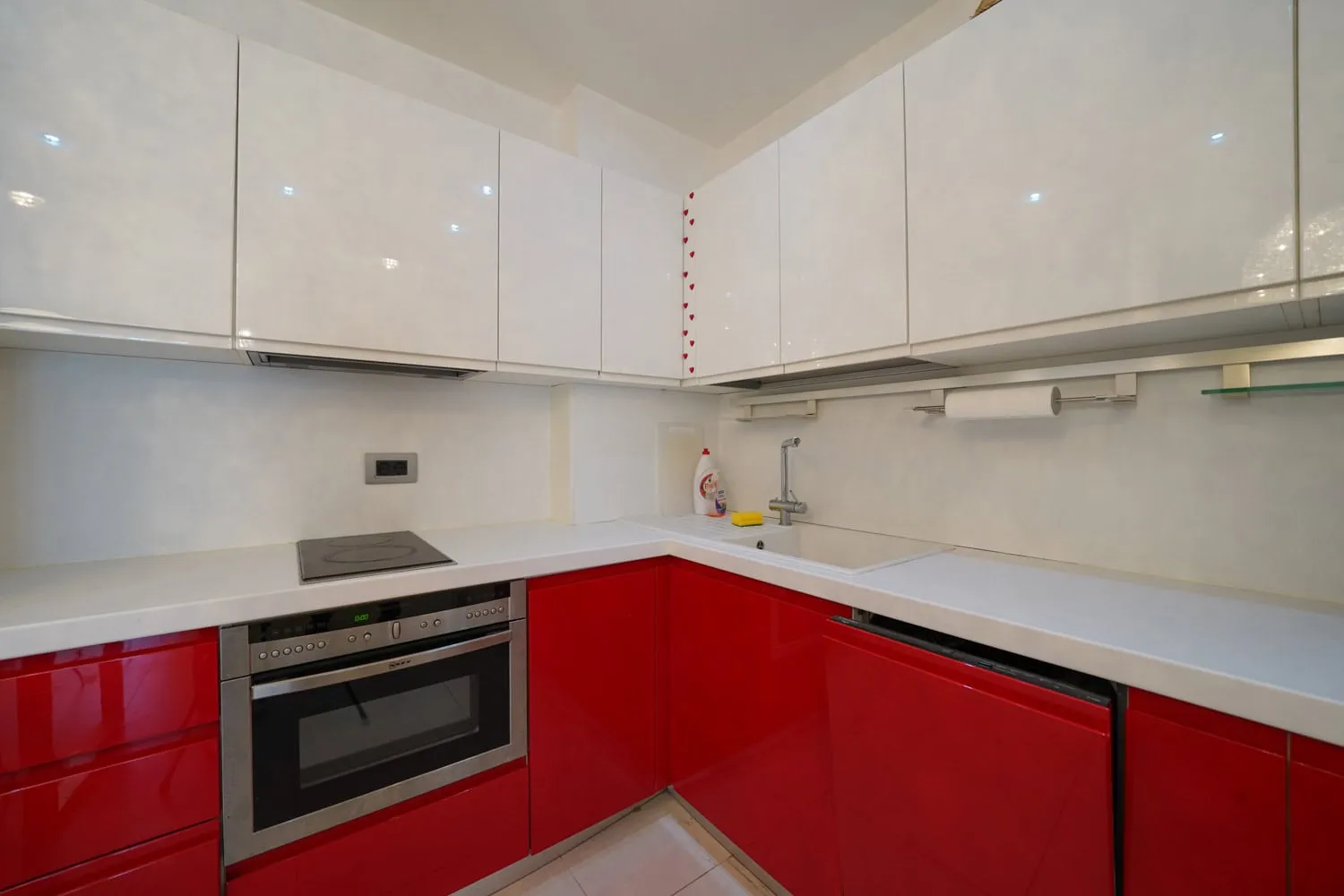 Moderne Küche mit roten und weißen Fronten in einer Wohnung in Budva, Montenegro: Einbaugeräte und helle Arbeitsplatte.