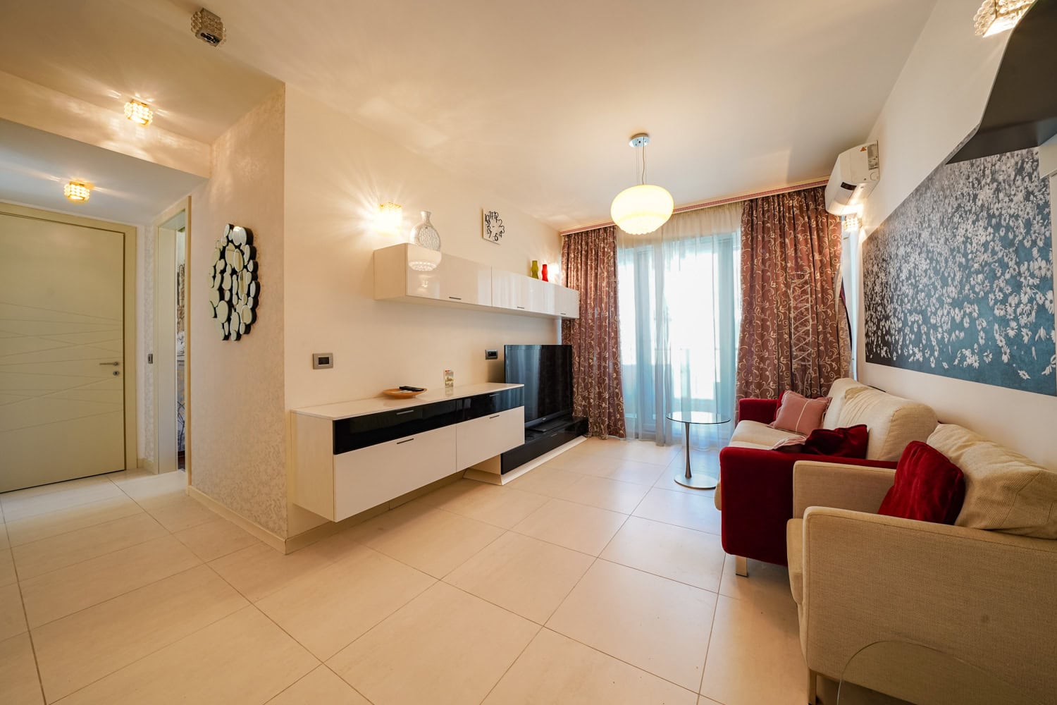 Modernes Wohnzimmer mit weißen Möbeln und rotem Sofa in einer Wohnung, Budva, Montenegro. Helles Interieur mit Panoramafenster.