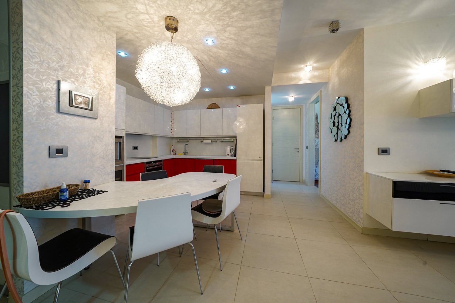 Moderne Wohnküche mit weißer Einbauküche in einer Wohnung in Budva, Montenegro: Essbereich und stilvolle Beleuchtung.