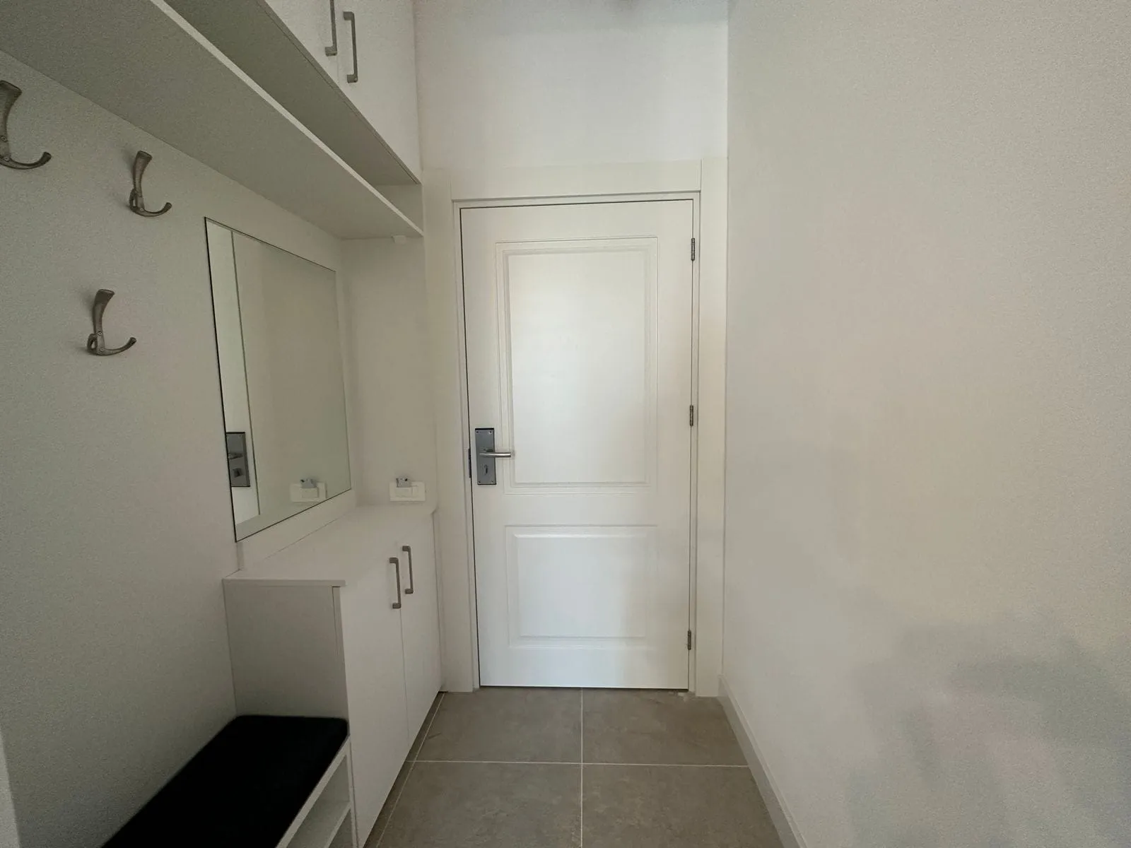 Entryway featuring a white door, wall mirror, coat hooks, storage cabinet, and black bench on tile floor.