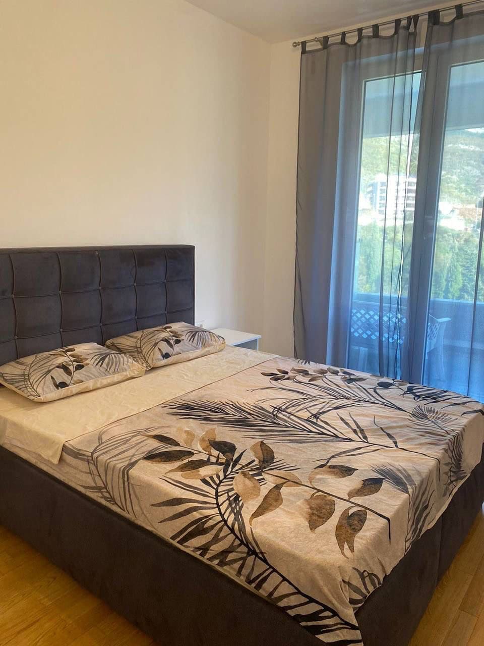 Sypialnia z łóżkiem podwójnym, tekstyliami w roślinne wzory i panoramicznym oknem w apartamencie w Bečići, Czarnogóra