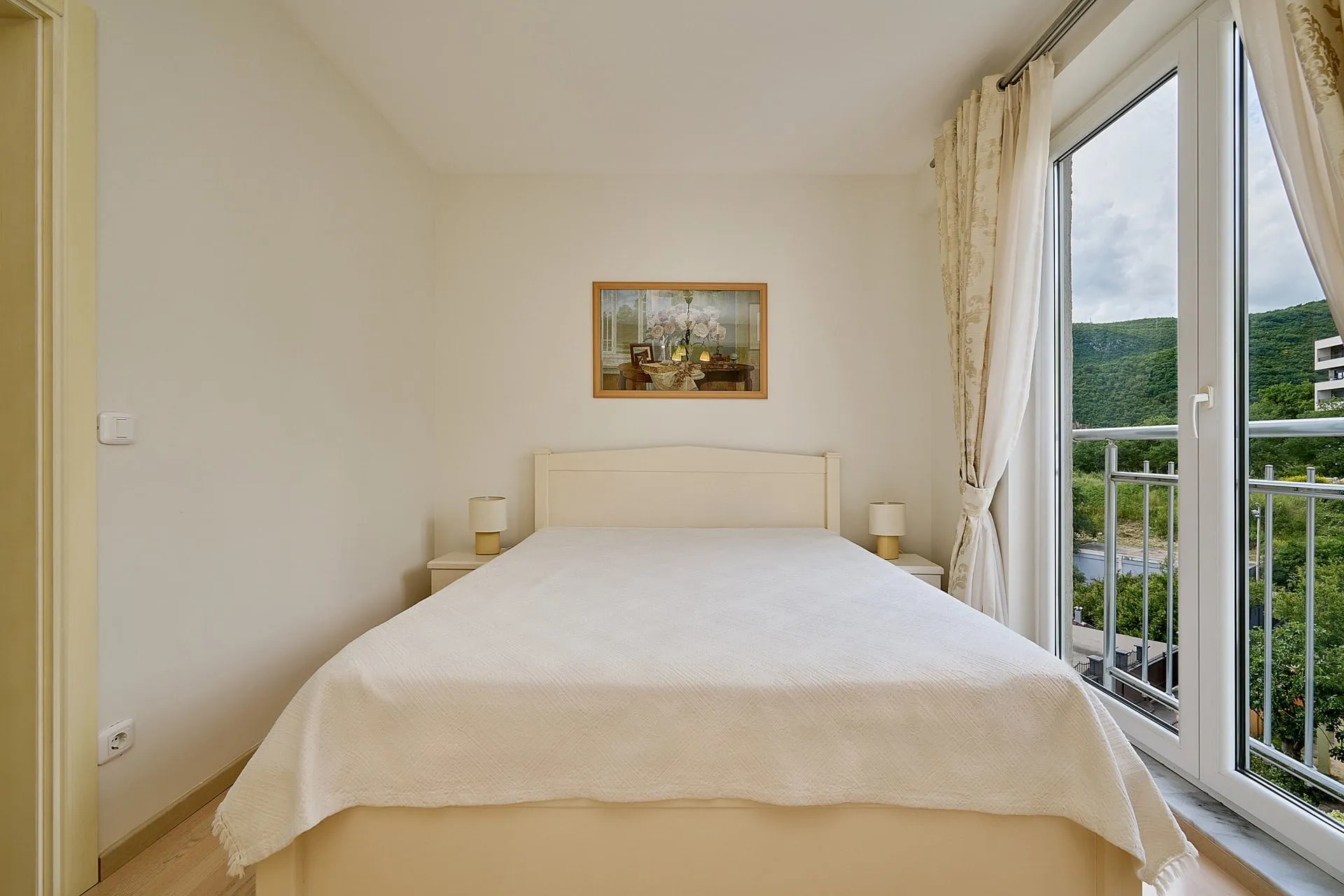 Helles Schlafzimmer mit Doppelbett und Zugang zum Balkon mit Bergblick in einer Wohnung, Bečići, Montenegro.
