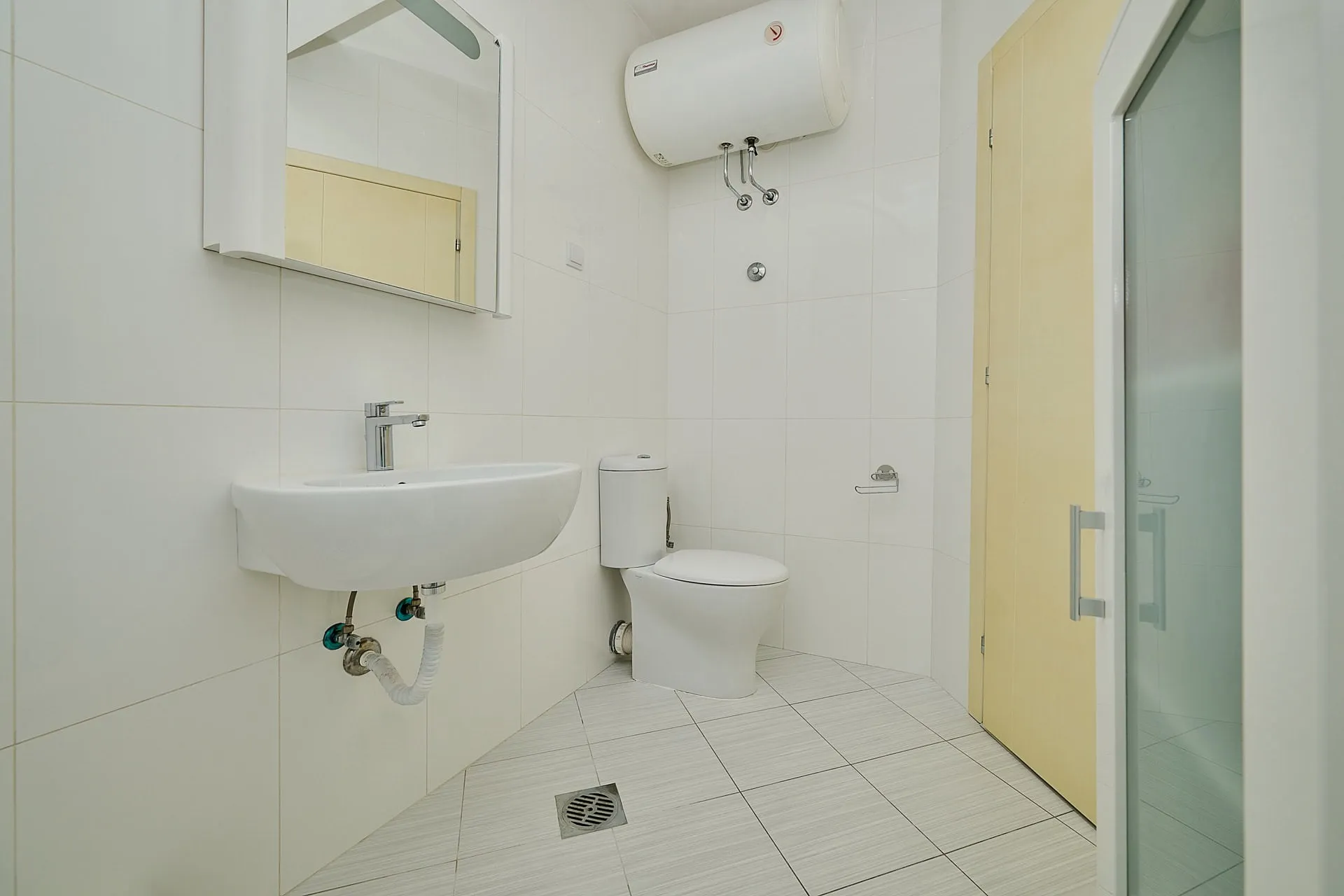 Helles Badezimmer in einer Wohnung in Bečići, Montenegro: weiße Fliesen, Sanitäranlagen, Boiler und Duschkabine.