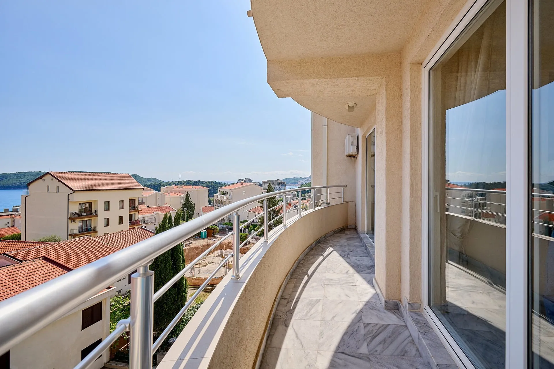 Geräumiger Balkon mit Marmorboden und Blick auf das Meer und die Stadt Bečići, Montenegro. Wohnung mit Panoramaverglasung.