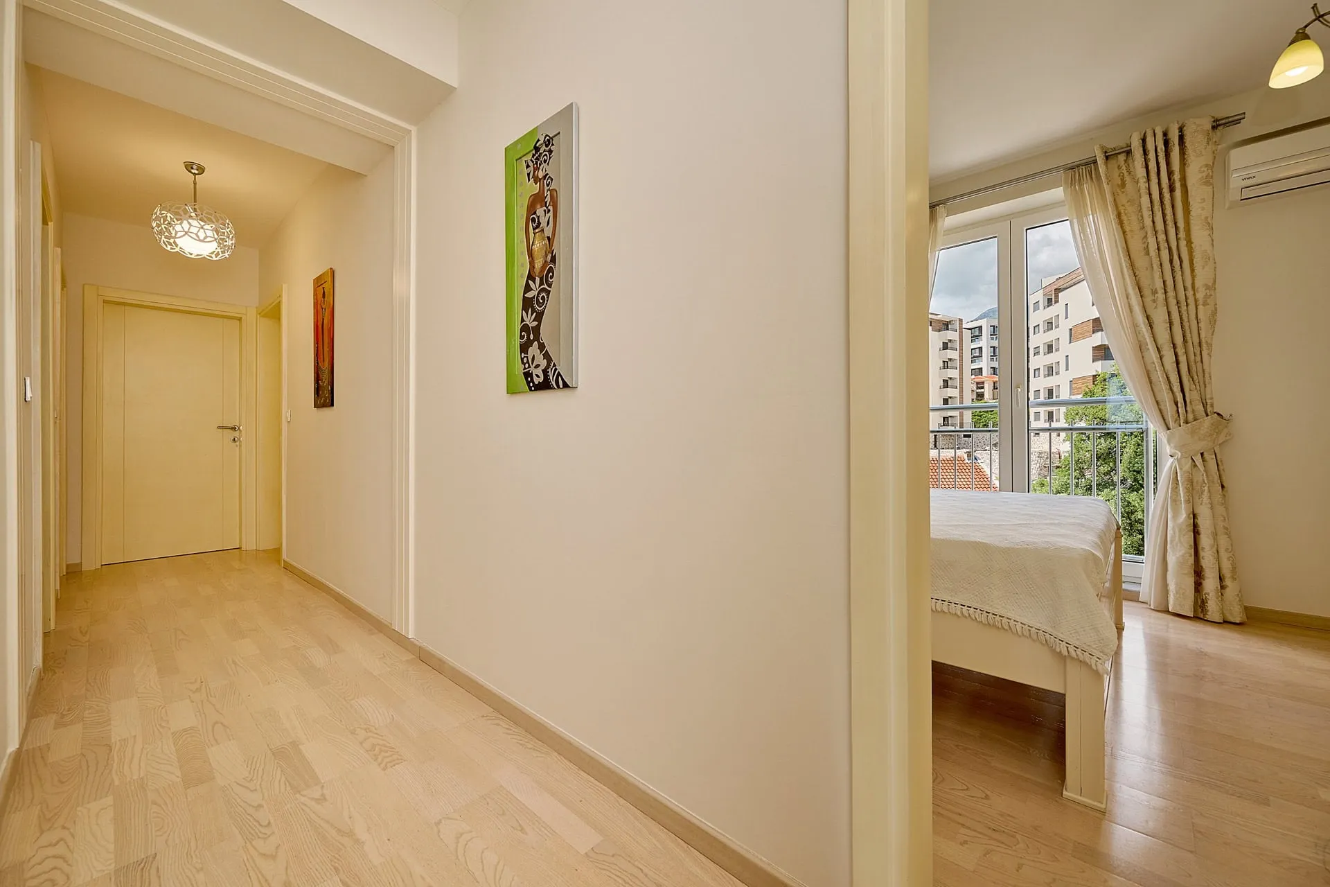Heller Flur und Schlafzimmer mit Zugang zum Balkon in einer Wohnung in Bečići, Montenegro: Parkett, Dekor und Blick auf die Stadt.