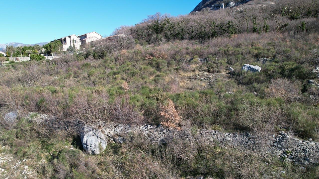 Baugrundstück in Blizikuće, Montenegro: hügeliges Gelände mit Steinmauerwerk und Bergblick.