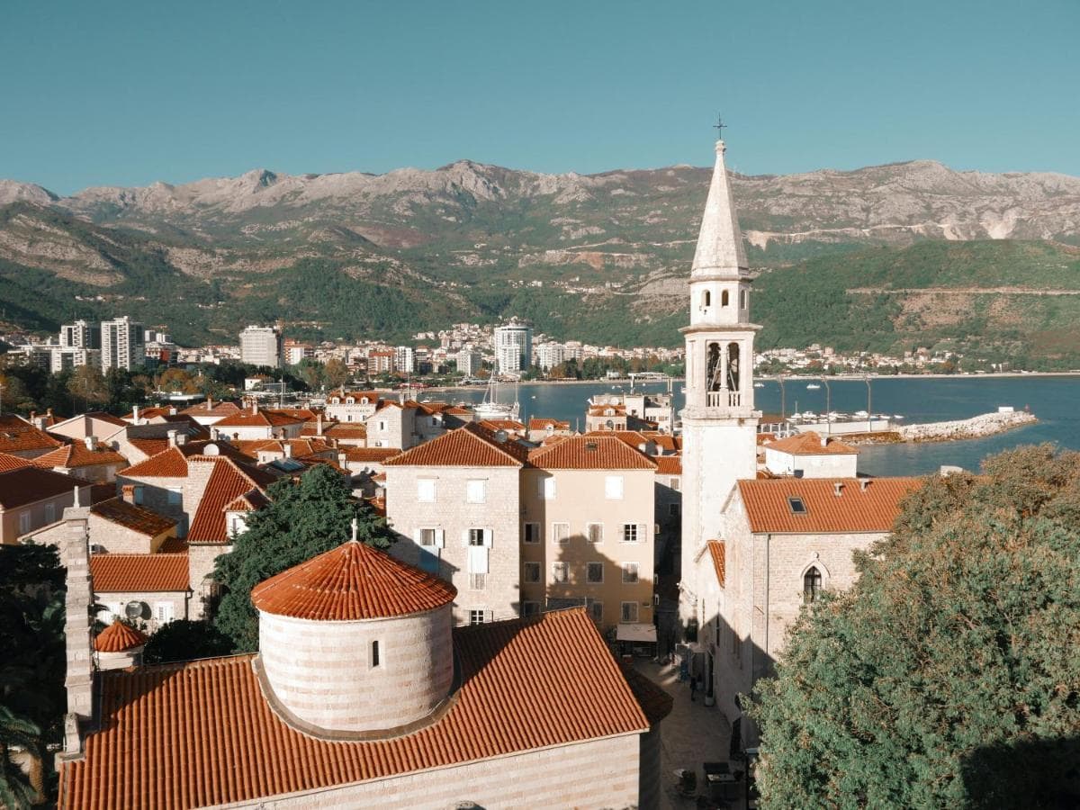 Panoramablick auf die Altstadt von Budva, Montenegro: Ziegeldächer, eine Kirche und die Meeresbucht vor Bergkulisse.