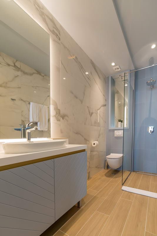 Modernes Badezimmer in einem Hotel in Budva, Montenegro: Marmoroptik, Duschkabine und stilvoller Waschtischunterschrank mit Waschbecken.