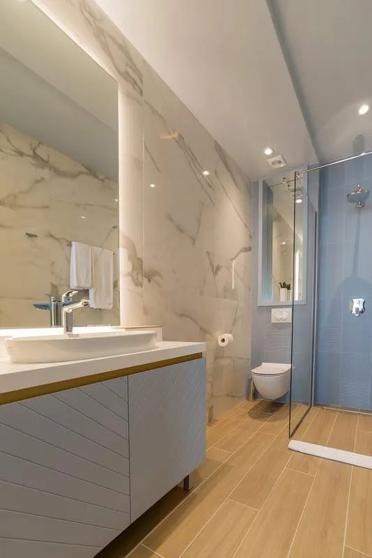 Modernes Badezimmer in einem Hotel in Budva, Montenegro: Marmoroptik, Duschkabine und stilvoller Waschtischunterschrank mit Waschbecken.