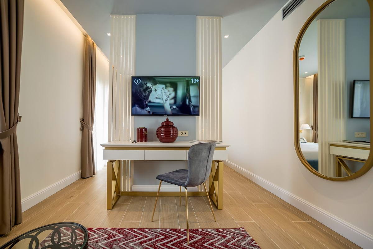 Modernes Schlafzimmer in einem Hotel in Budva, Montenegro: Schreibtisch, TV, stilvolle Dekoration und großer Spiegel mit goldenem Rahmen.