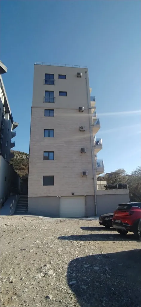 Modernes Wohnhaus mit Balkonen und Parkplatz in Bečići, Montenegro: Ansicht der Gebäudefassade mit angrenzendem Grundstück.