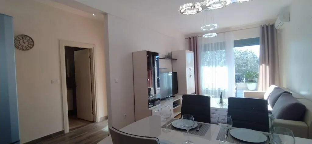 Modernes Wohnzimmer mit Essbereich in einer Wohnung, Bečići, Montenegro: helle Möbel, TV-Bereich und Zugang zum Balkon.