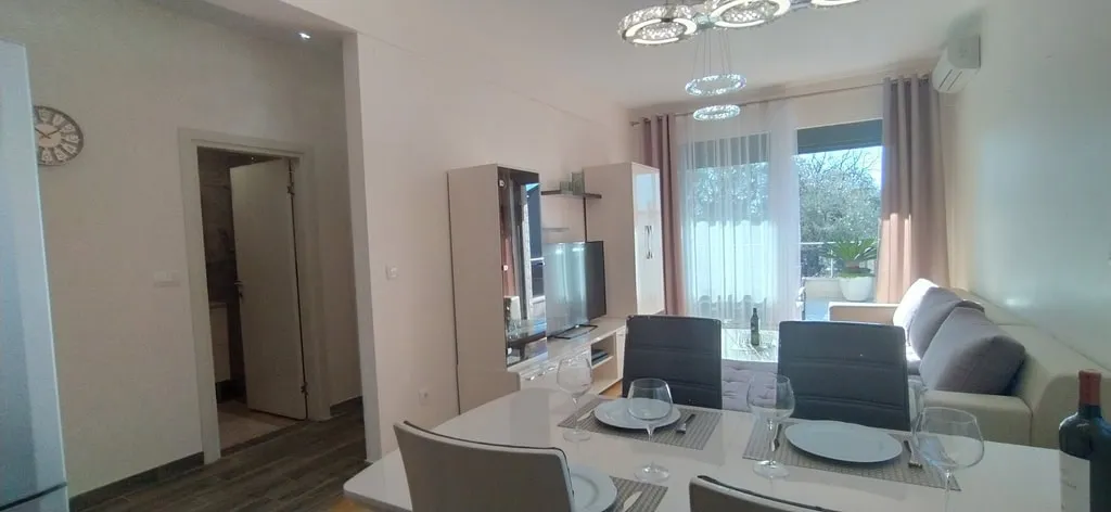 Modernes Wohnzimmer mit Essbereich in einer Wohnung, Bečići, Montenegro: helle Möbel, TV-Bereich und Zugang zum Balkon.